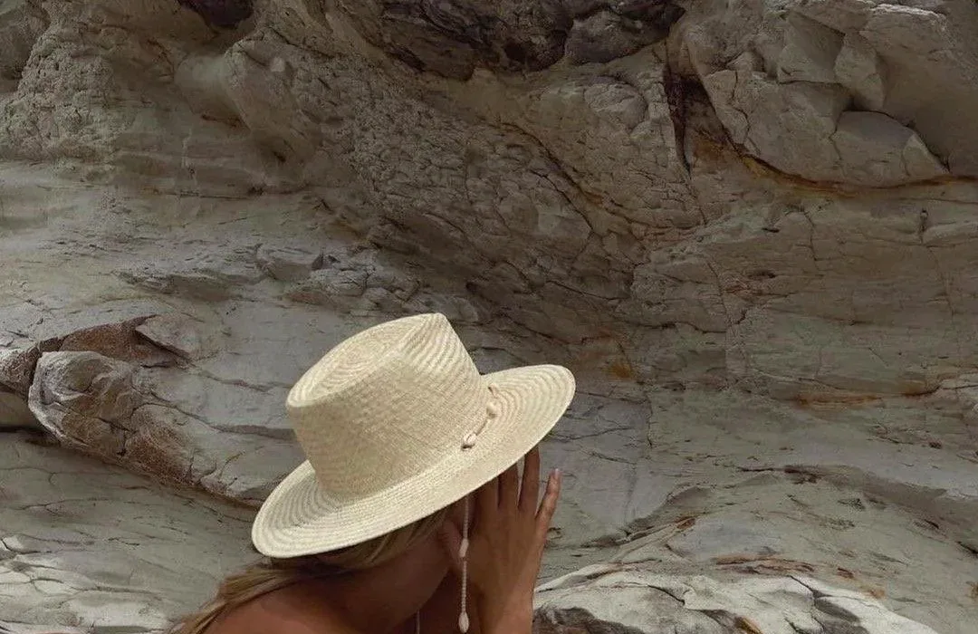 A woman in a wide-brimmed straw hat resting against pale coastal rock